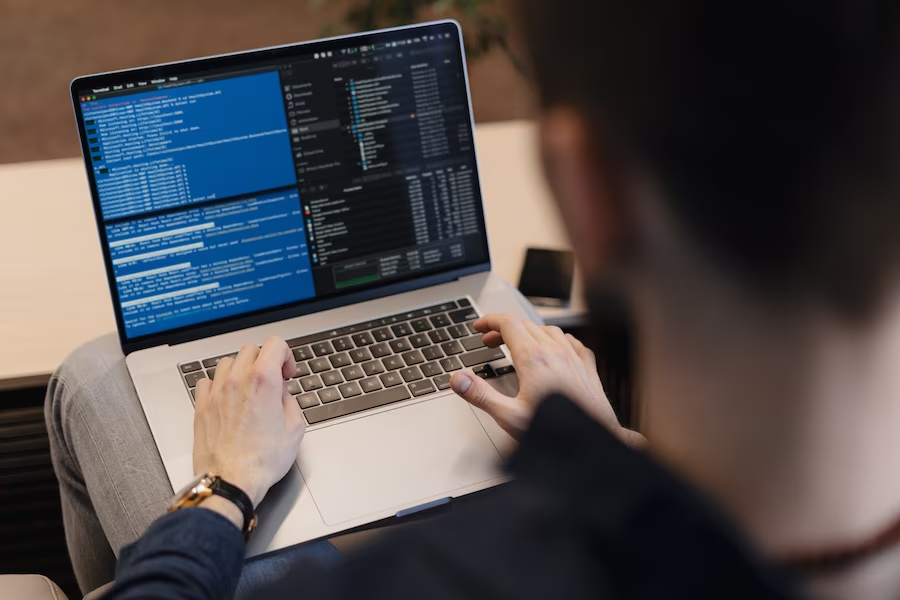 A man sitting with a laptop on his lap, focused on writing computer code